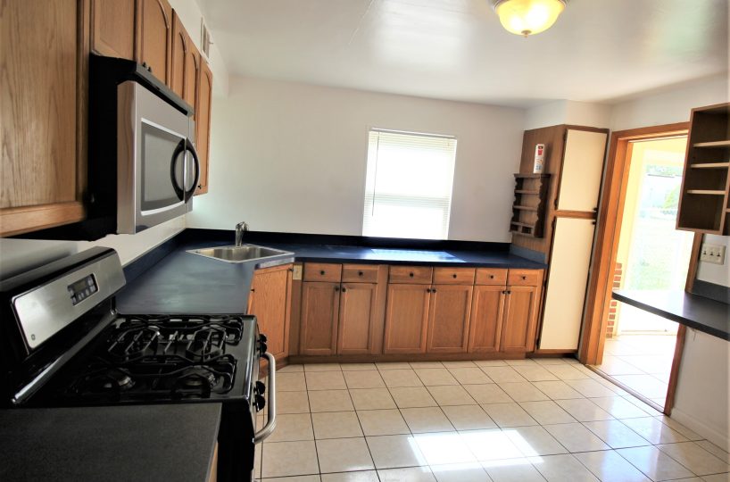 218 Riverview Ave Kitchen with large floor tiles, oven, microwave, black countertops, wood cabinets and window with blinds.