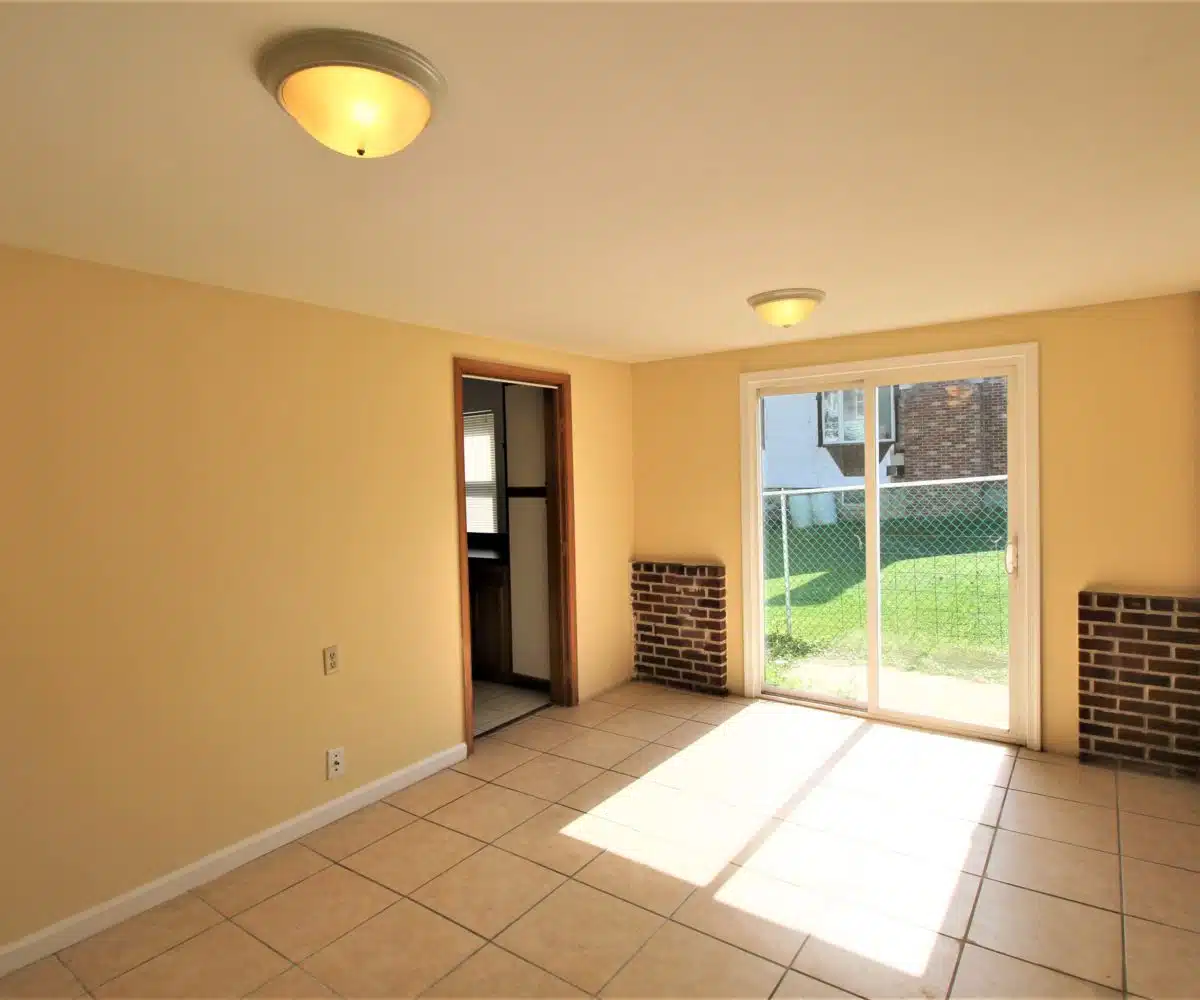 Family room with sliding glass door, large square floor tiles, brick walls, window and ceiling light.