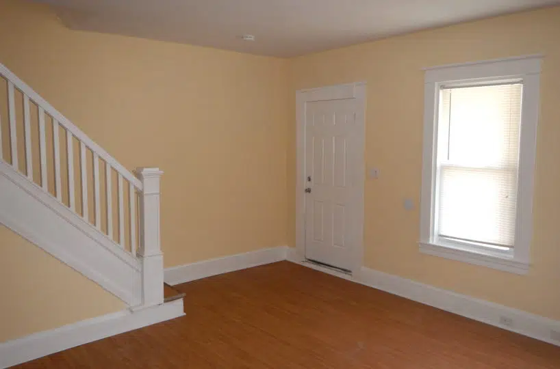 Living Room with wood flooring, yellow walls, window with white blinds and staircase leading upstairs with white guardrail.