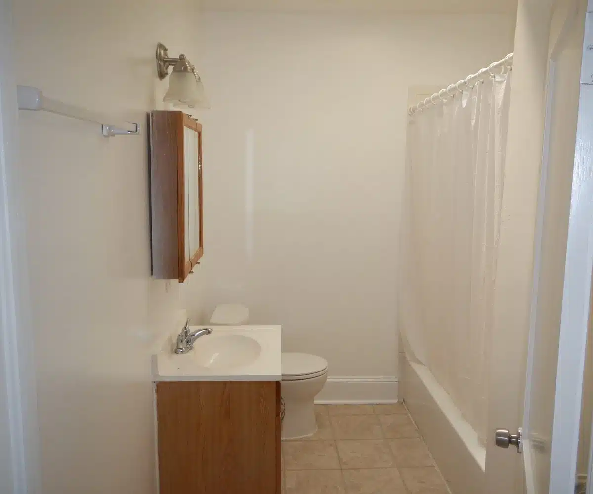 Bathroom with large beige floor tiles bath vanity, toilet, medicine cabinet, and bathtub with white curtain.