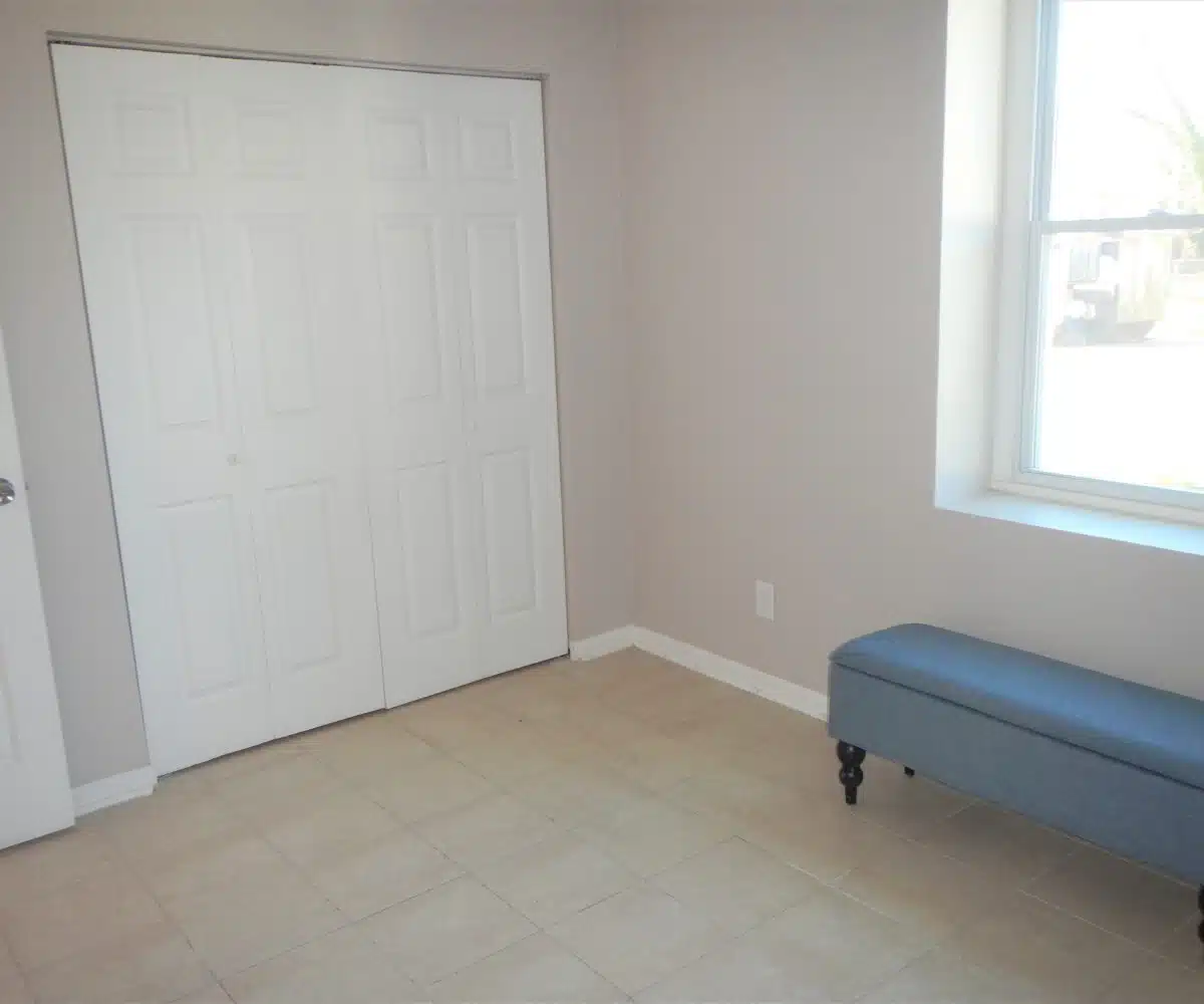 Roslyn Bedroom with window, blue bench and white closet doors.