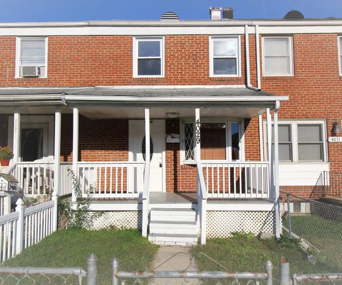 Red brick townhome with grass, white stairs, white guard railing and grey porch.