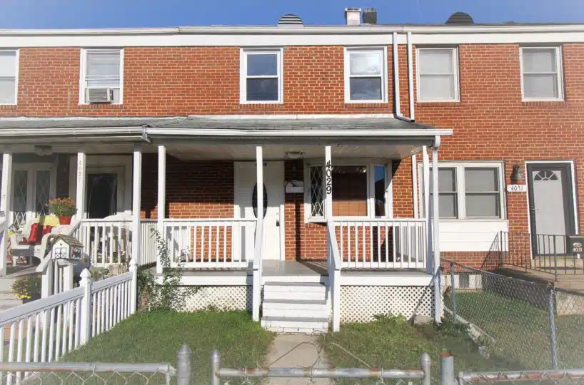 Red brick townhome with grass, white stairs, white guard railing and grey porch.