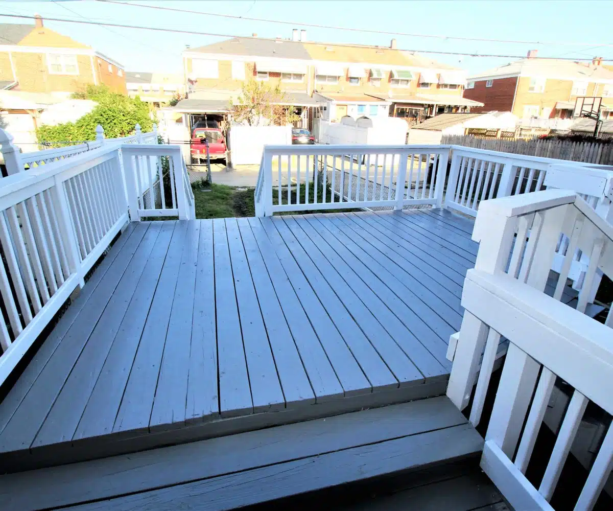 Wood porch with white guard railing and stairs leading to backyard.