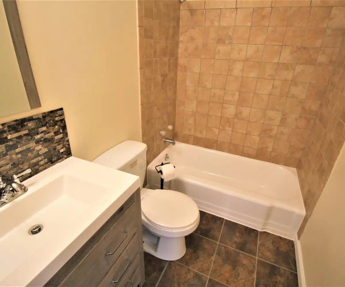 Fancy bathroom with freestanding bath vanity, toilet, and red tiled bathtub.