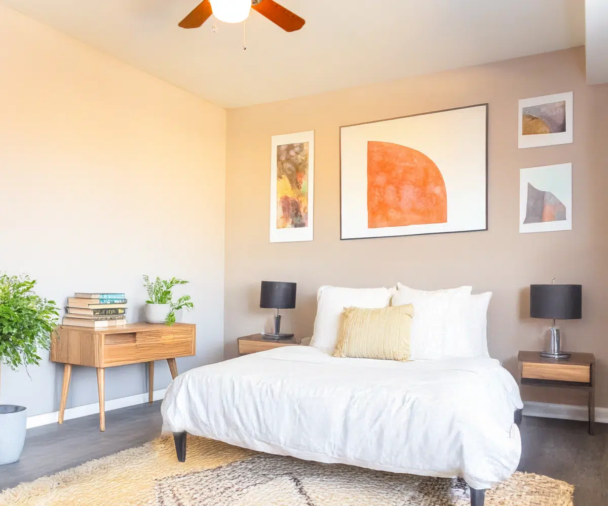 Bedroom with white bed, two table lamps, ceiling fan and two plants.