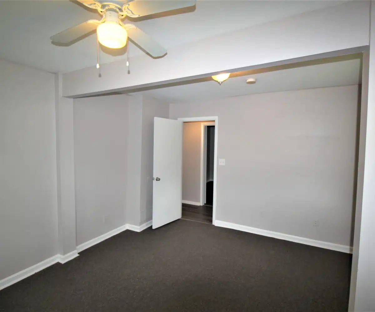 Brown carpeted bedroom with grey walls and a ceiling fan.