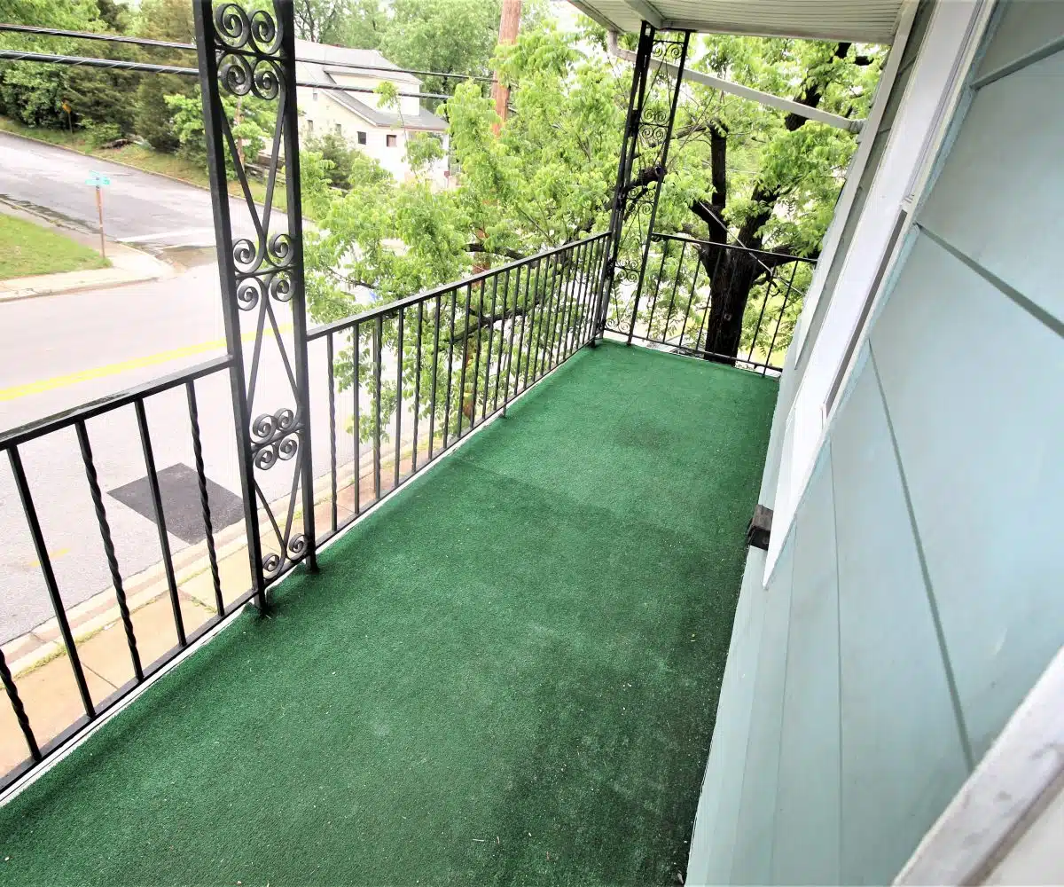Green carpeted porch with black metal hand railing overlooking trees.