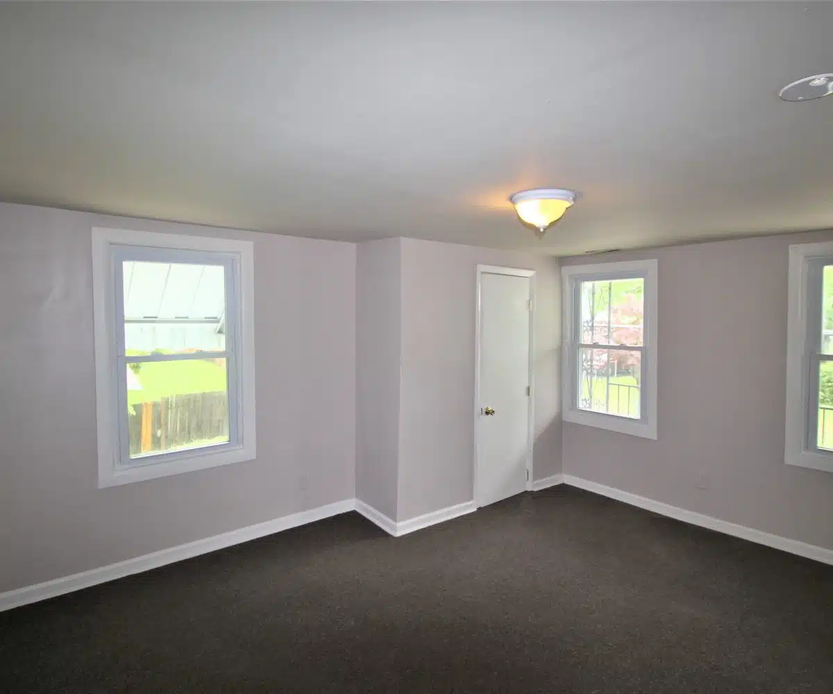 Bedroom with brown carpet three windows and ceiling light.
