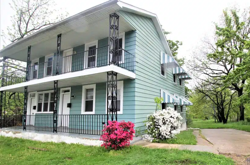 Home with blue siding, metal hand railing, green lawn and flowers.