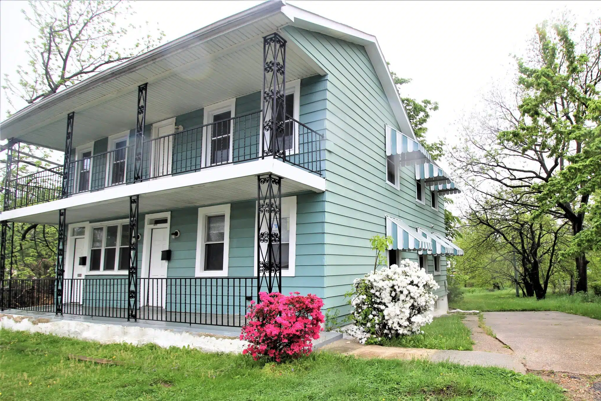 Home with blue siding, metal hand railing, green lawn and flowers.