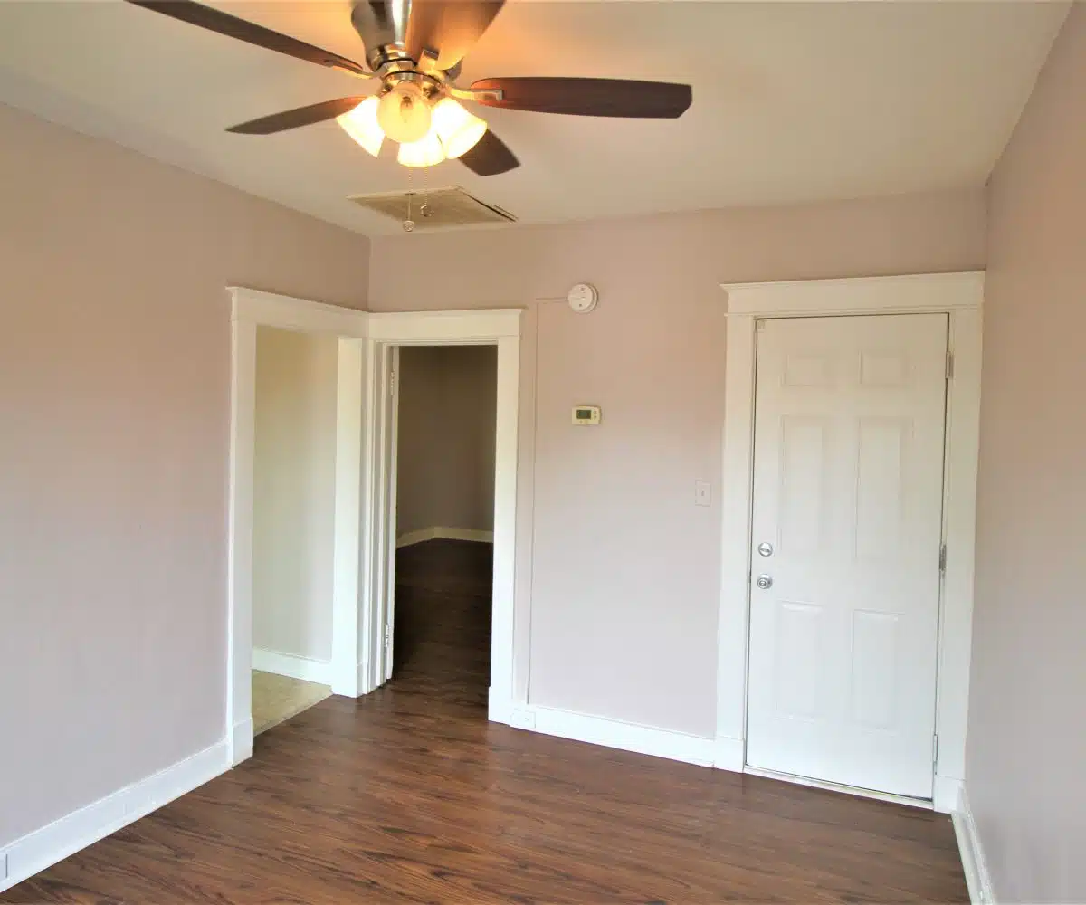 Living room with pink walls, white molding, wood flooring and ceiling fan.