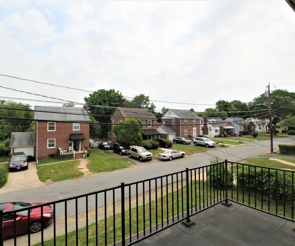 Black front porch with metal railing and view of street with parked cars and home across the street.