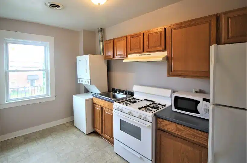 Kitchen with window, washer-dryer unit, sink, oven, fridge, microwave and wood cabinets.