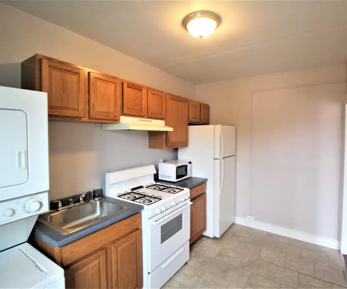 Kitchen with wood cabinets, stainless steel sink, washer and dryer unit, oven and fridge.