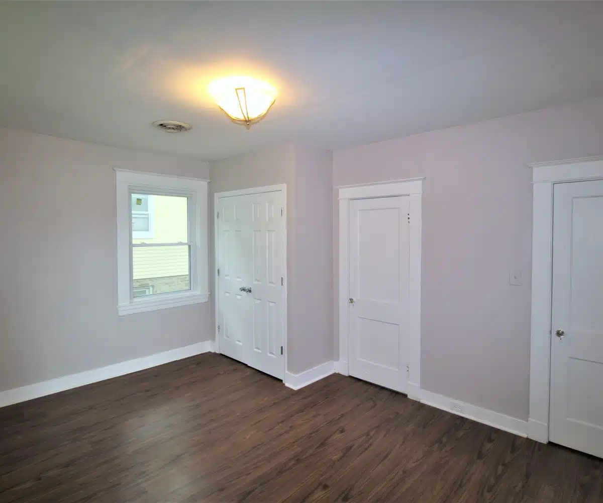 Room with wood flooring, white doors, and a window.