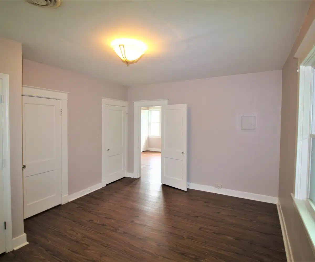 Room with pink walls, wood flooring, white doors and ceiling light.