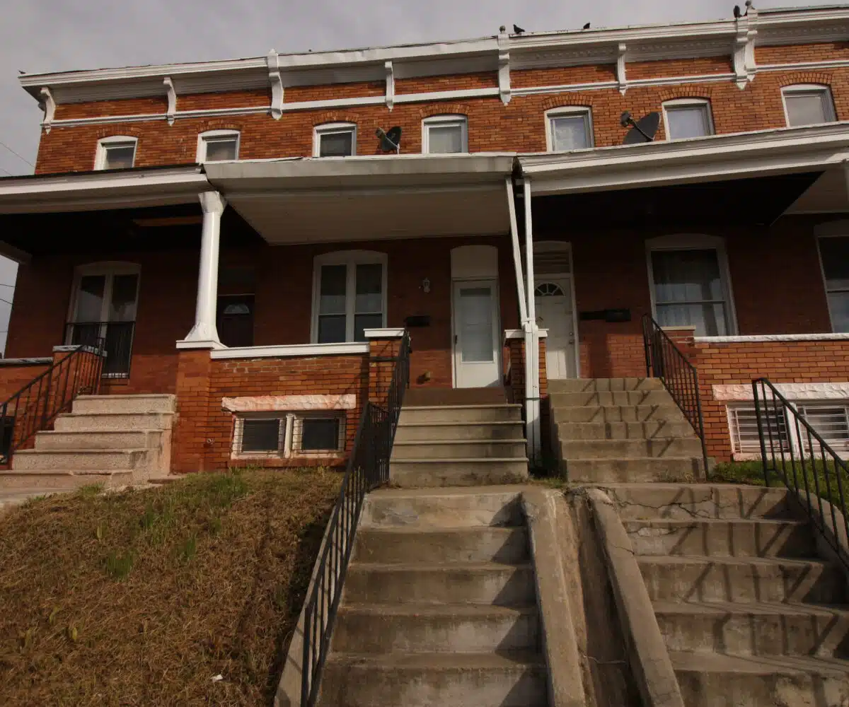 Red brick townhome with concrete stairs and white front door.