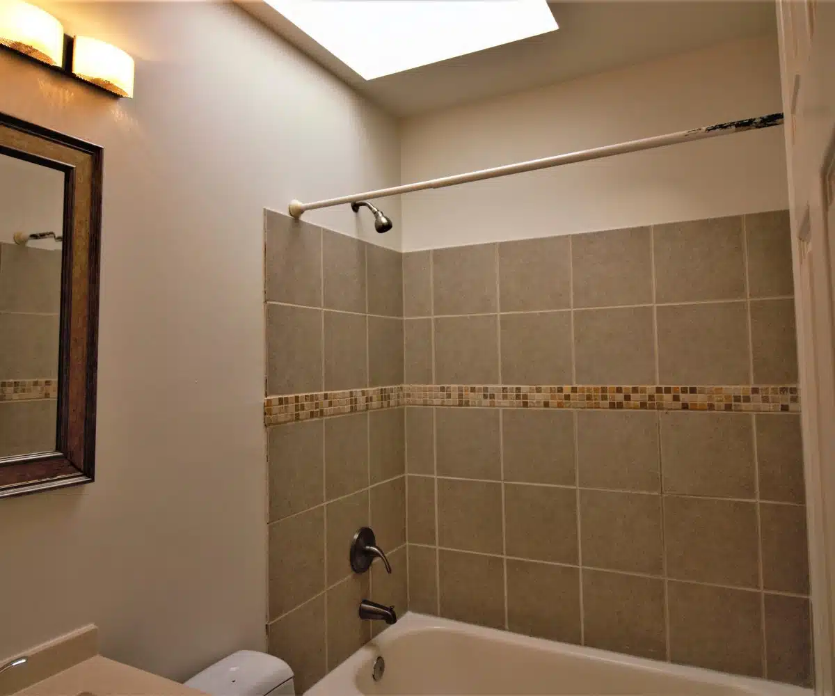 Bathroom with sink, brown framed wall mirror, and bathtub with grey wall tiles.