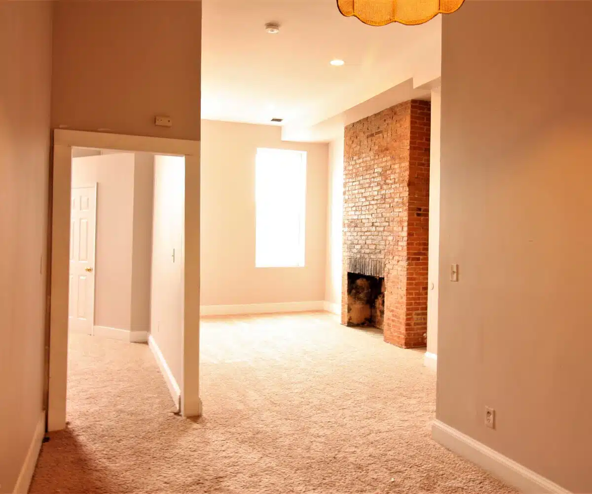 Carpeted living room with fireplace and window and a carpeted hallway.
