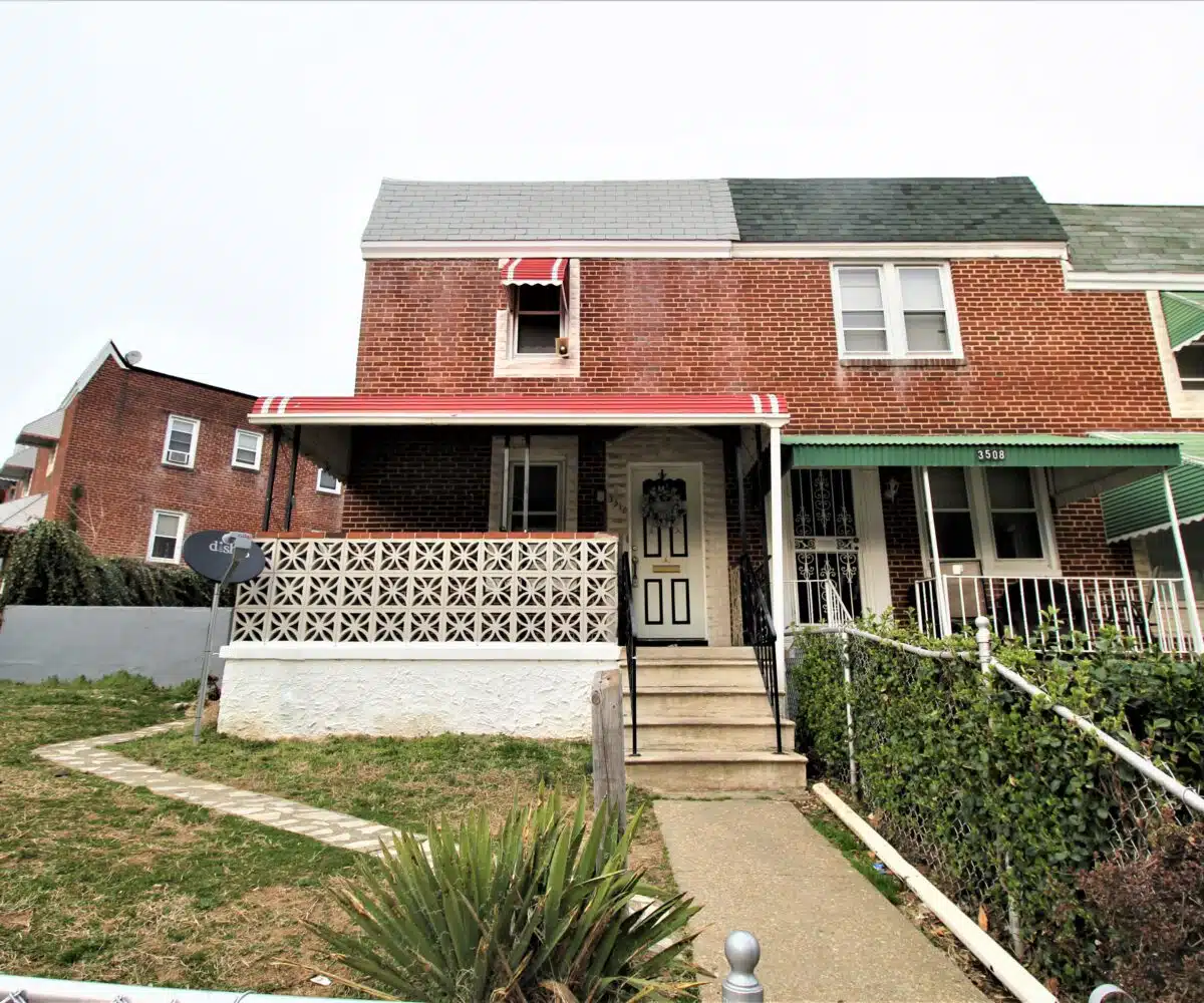 Red brick townhome with concrete front path, stairs and black and white front door.