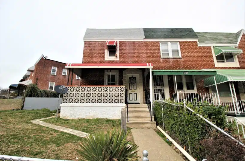 Red brick townhome with concrete front path, stairs and black and white front door.