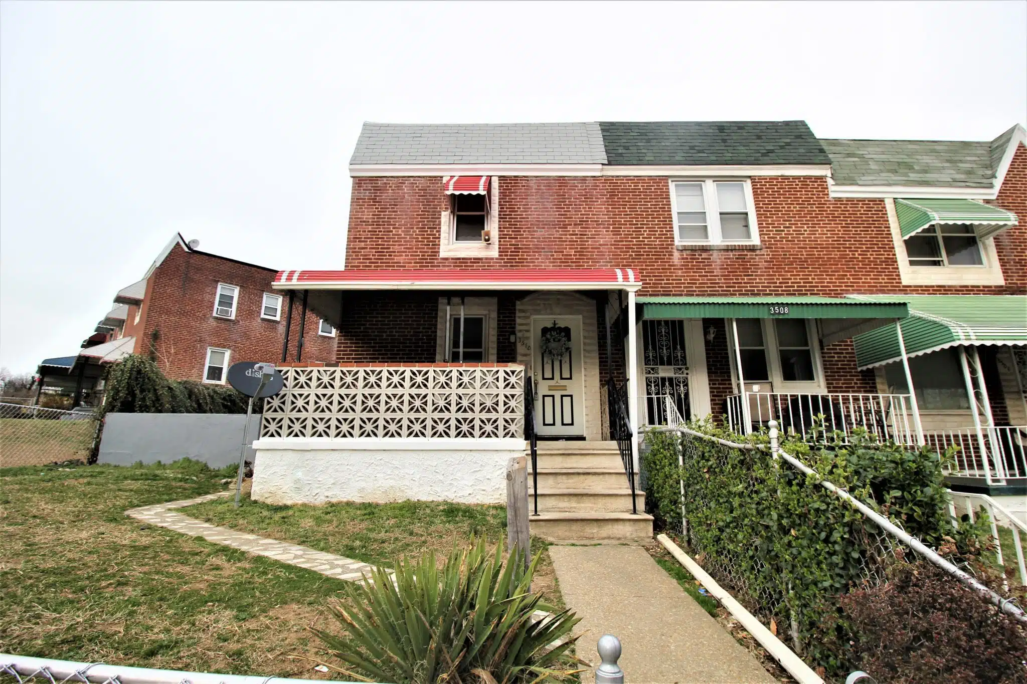 Red brick townhome with concrete front path, stairs and black and white front door.
