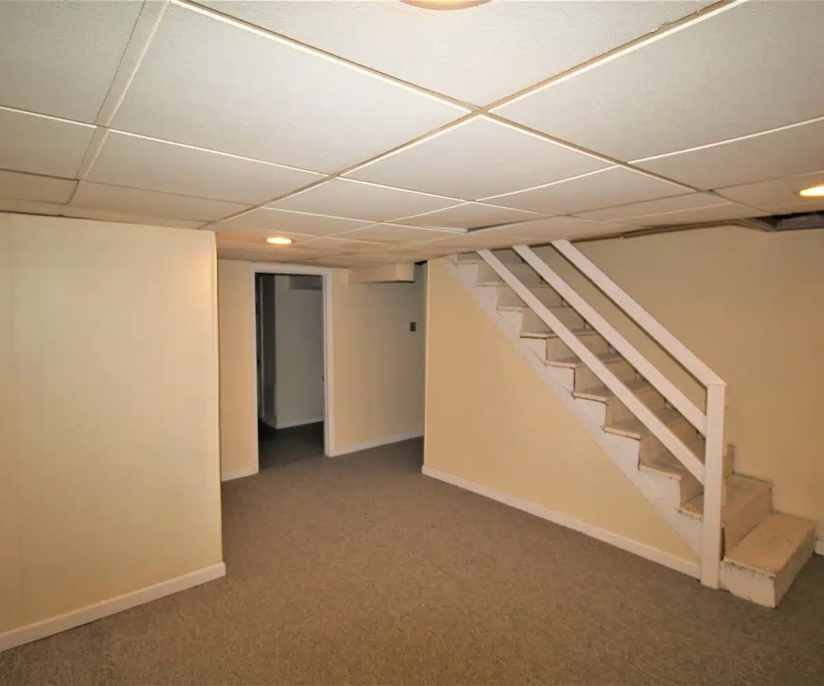 Brown carpeted basement with yellow walls, recessed lighting and wood staircase leading upstairs.