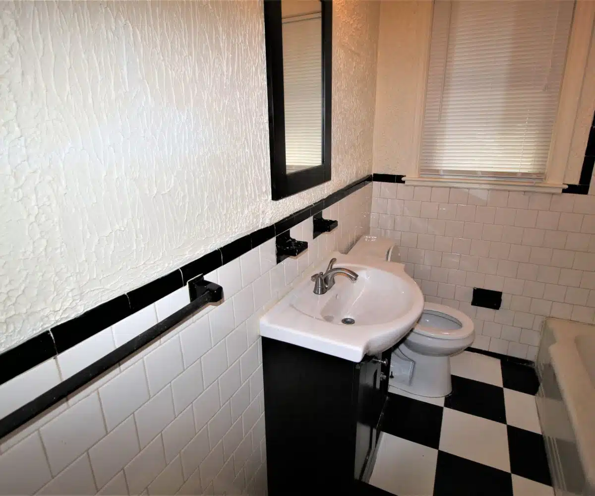 Bathroom with black and white floor tiles, sink, mirror, toilet and bathtub.