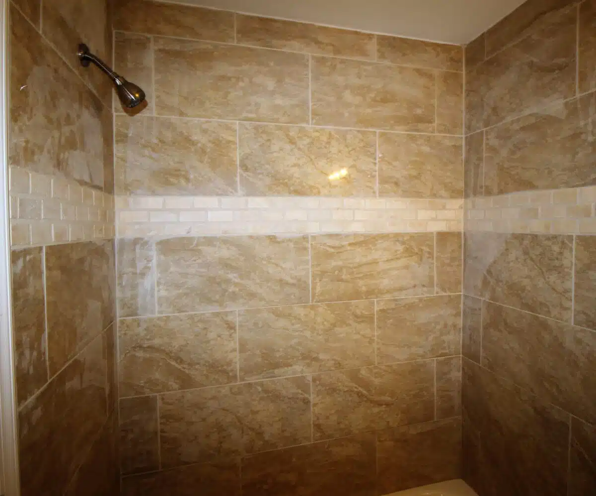 Bathtub with large brown wall tiles and silver showerhead.