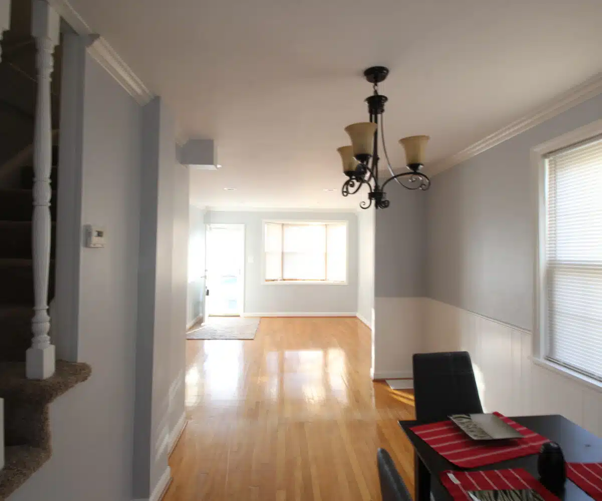 Living room and dining room with wood flooring, hanging light fixture, black table and chairs.