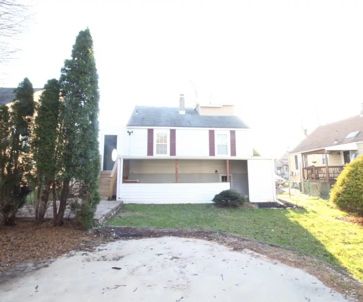 Backyard of home with white siding, red window shutters, and green grass.