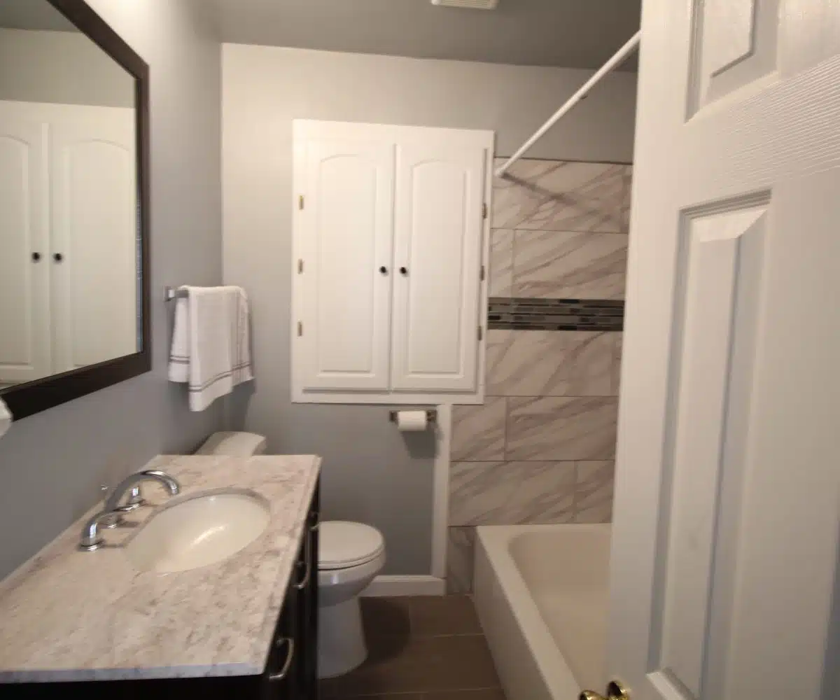 Bathroom with red floor tiles, sink with cabinet, wall mirror, toilet and bathtub.