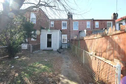 Fenced-in backyard, concrete path, trees, and wood fence.