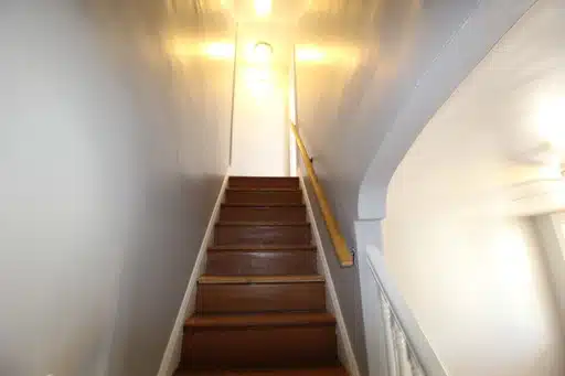 White stairwell with wood stairs leading upstairs and a hand rail.