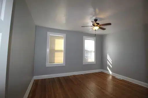 Bedroom with grey walls, windows, wood flooring and a ceiling fan.