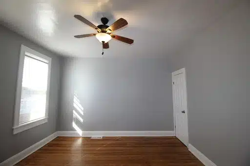 Bedroom with grey walls, wood floor, ceiling fan and a window with blinds.