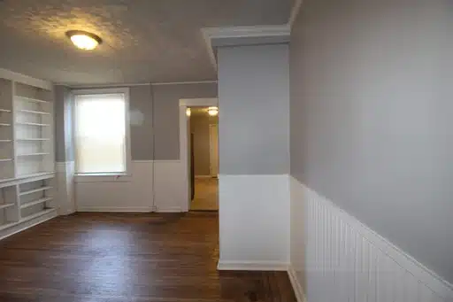 Living room with wood floor, grey and white walls, white shelves, window and ceiling light.