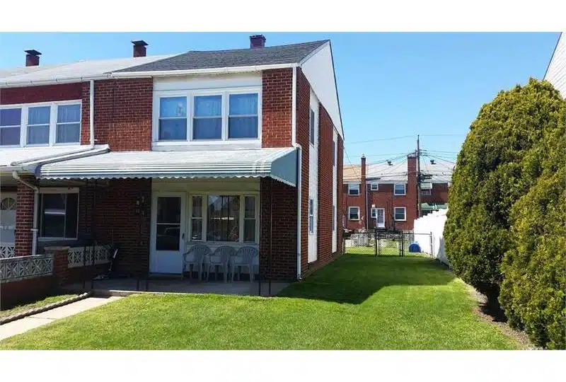 Red and white townhome with porch awning, white front door and grass lawn.