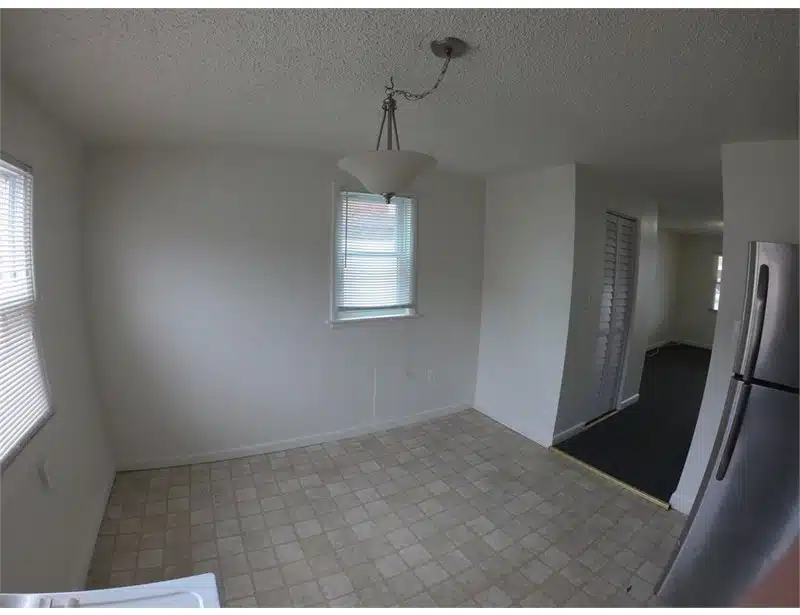 Kitchen with windows, hanging light fixture, square floor tiles and fridge.