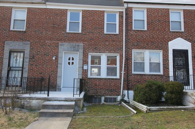 Red brick rowhome with windows and decorative front door.