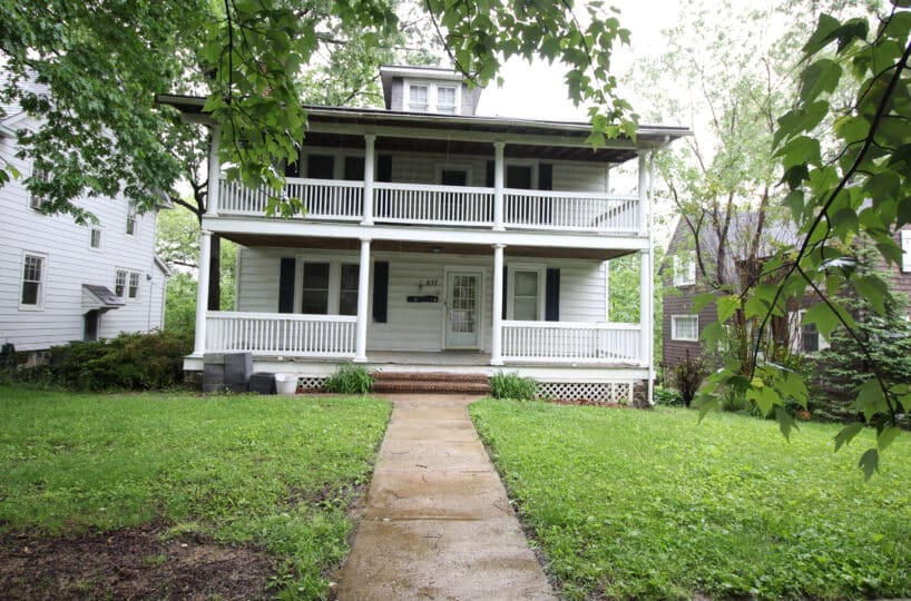 Two story home with white wooden fences surrounding the porch and upper balcony.