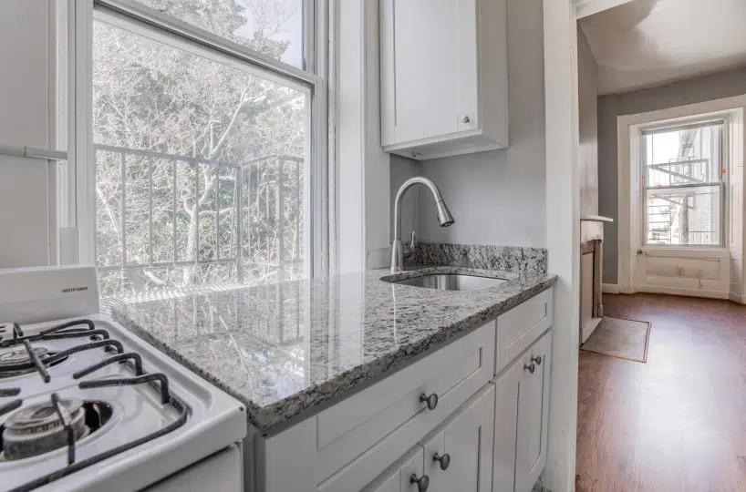 Kitchen with stove, sink and granite countertop and living room with hardwood floors.