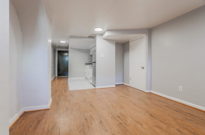 Grey living room and kitchenette with stove, fridge and white cabinets.