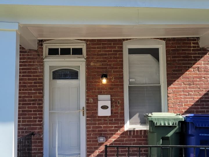 Red brick townhome with red porch, white front door and black metal fence.