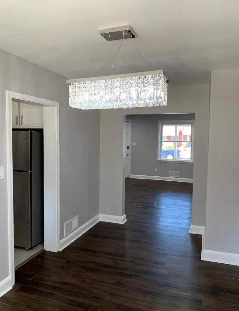 Grey walled dining room with hardwood floors and crystal chandelier.