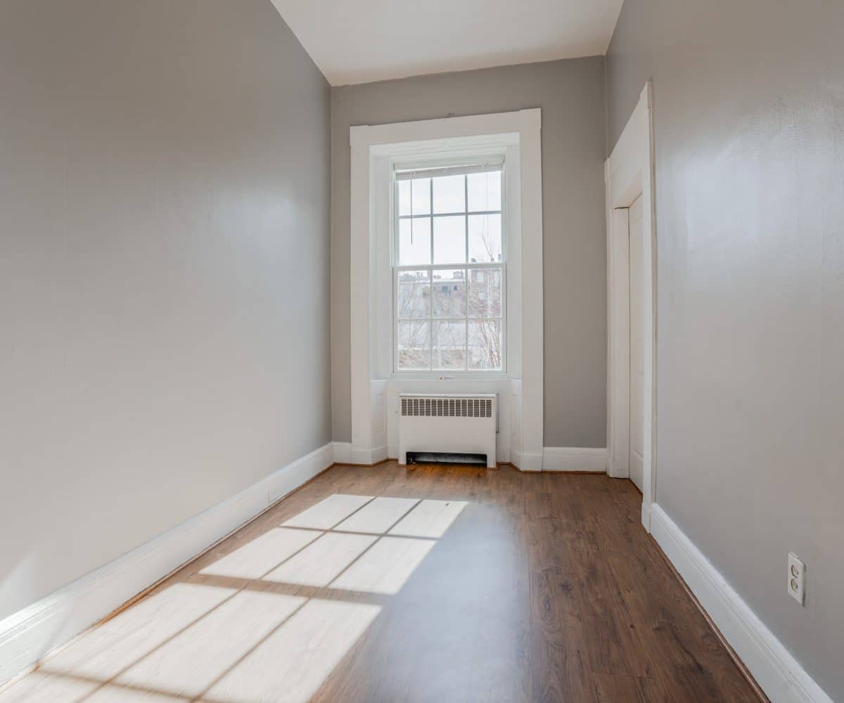 Sunny bedroom with large window, radiator, and grey walls.