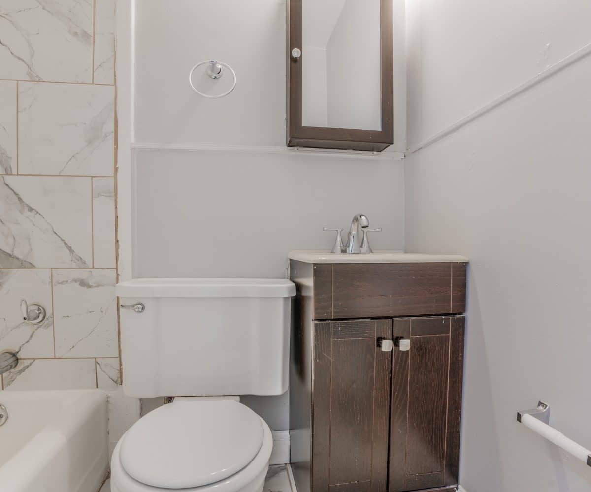 Bathroom with black and white tiled bathtub, toilet and sink with cabinet.