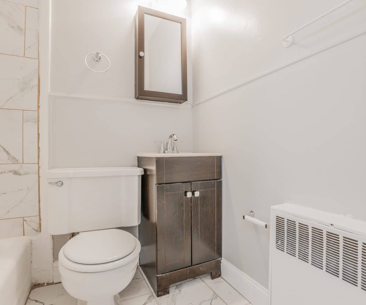 Bathroom with toilet, medicine cabinet and sink with wood cabinet.