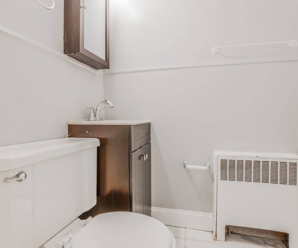 Bathroom with toilet, radiator, medicine cabinet, and sink with wood cabinet.